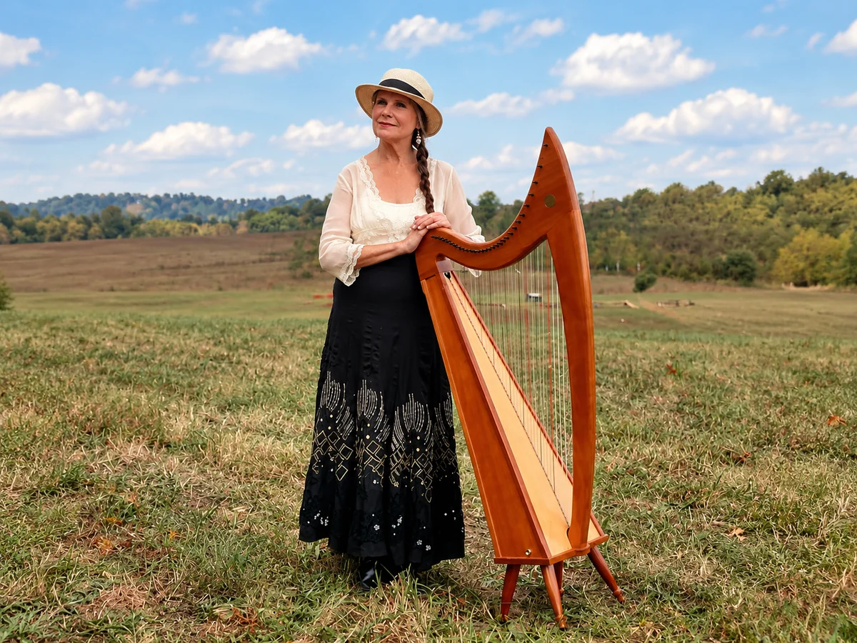 Sandra Morefield Parker standing beside her Celtic harp in an Appalachian meadow